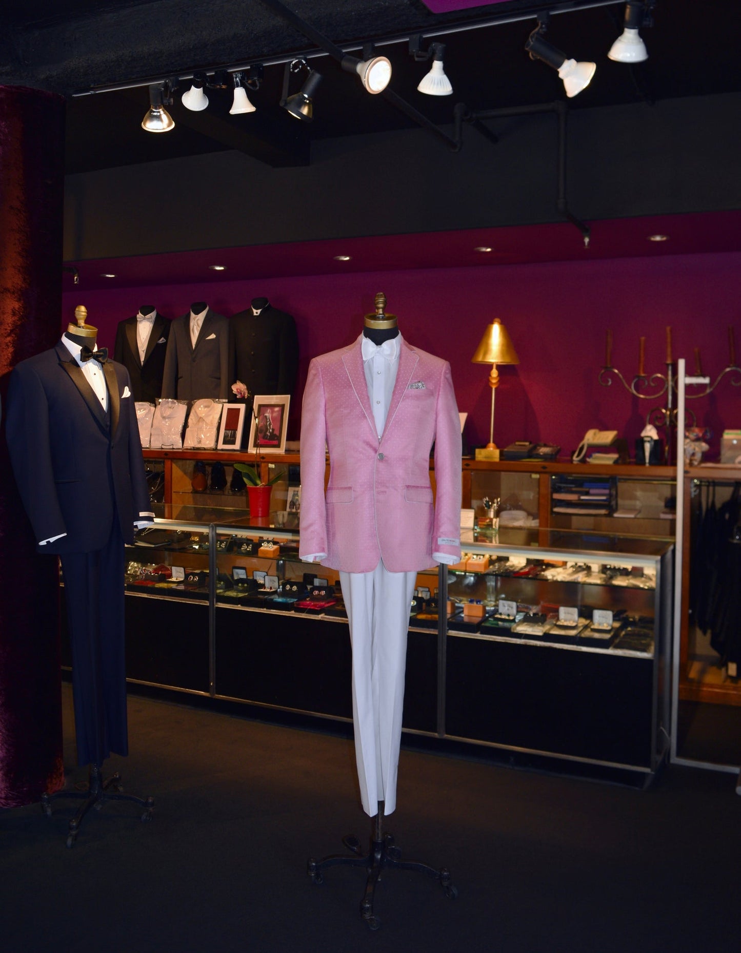 Full length mannequin wearing a pink dinner jacket with white pants and white bowtie on display inside a tuxedo shop