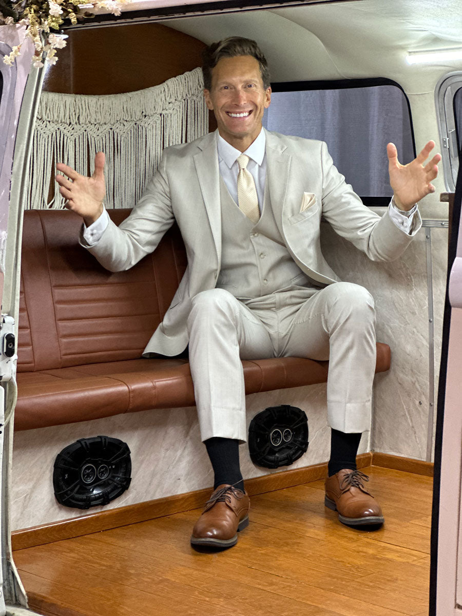 Man wearing a slim fit tan suit while sitting in the back of a vintage van at a wedding reception.