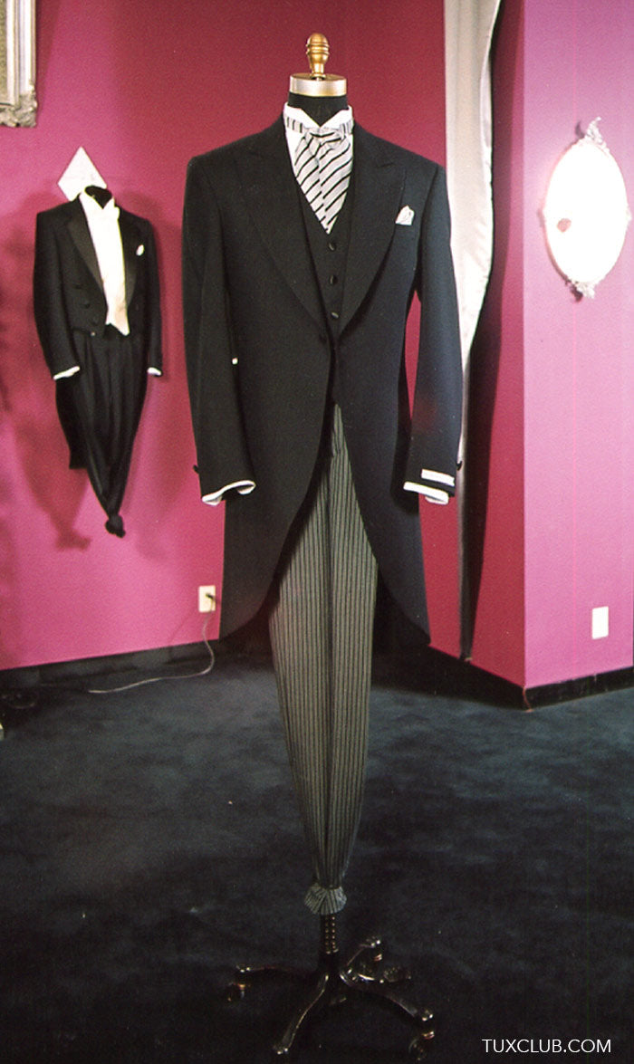 Black cutaway morning suit on a mannequin against a pink wall with another tuxedo in the background.