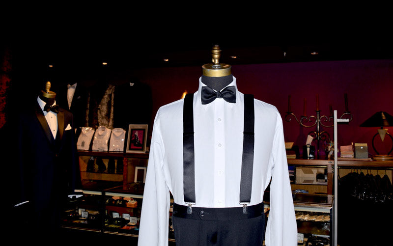 close up of mannequin wearing a formal outfit with a white shirt, black satin suspenders and bow tie at a tuxedo shop