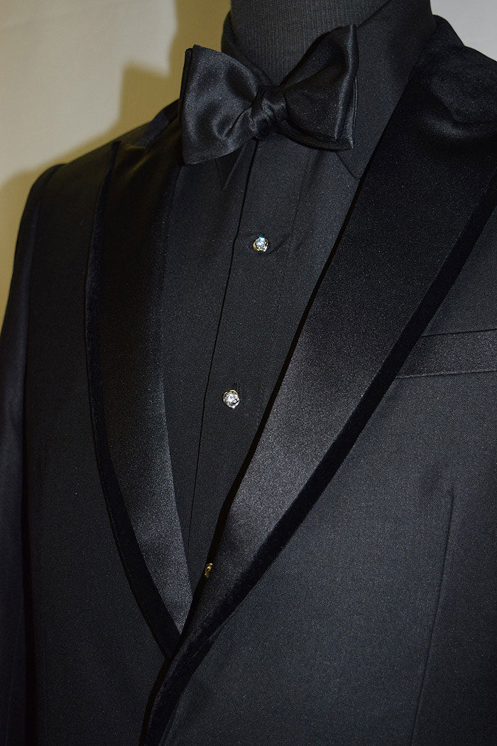 mannequin wearing a black tuxedo and black shirt and bowtie with cz cufflinks and studs against a white background