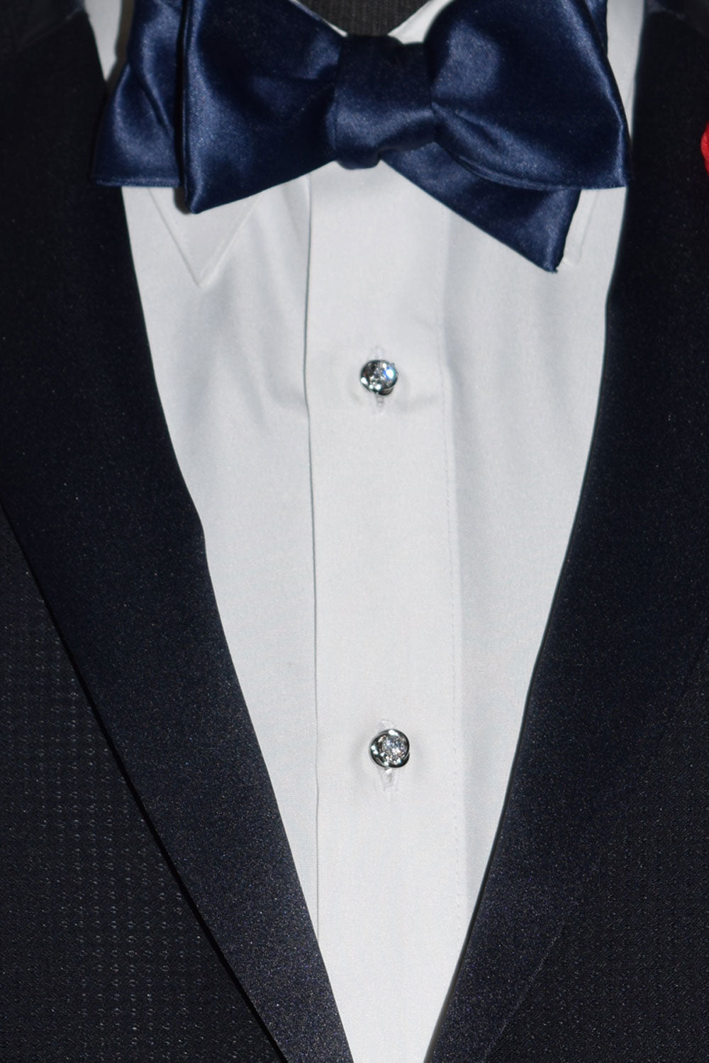 Close-up of a black tuxedo with a navy bow tie and white shirt wearing cubic zirconia cufflinks and studs