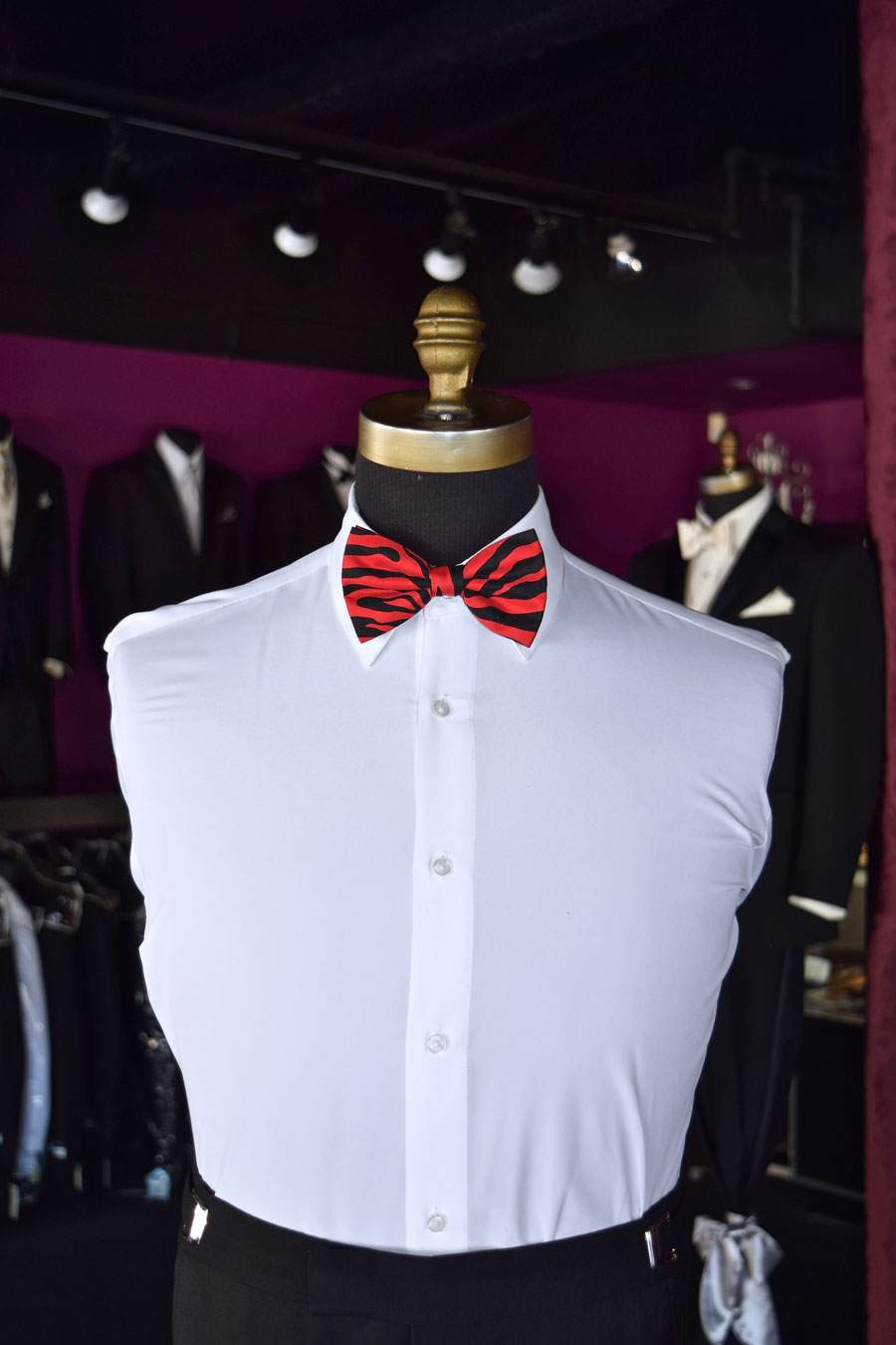 Mannequin wearing a white dress shirt with a crimson red and black zebra print bow tie in a tuxedo shop setting.