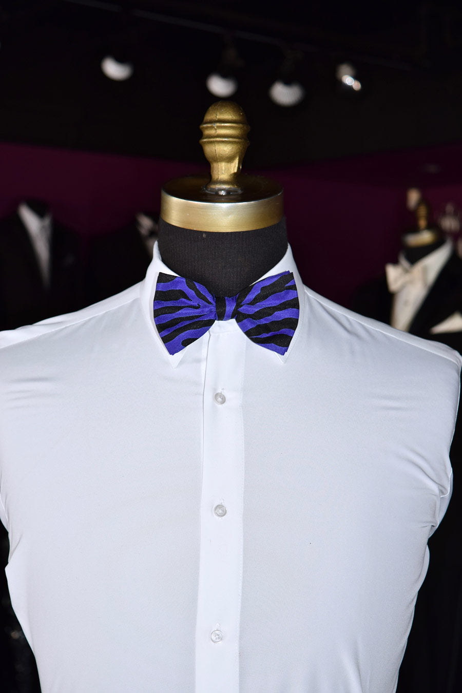 Mannequin wearing a white dress shirt with a purple and black zebra print bow tie against a dark background.