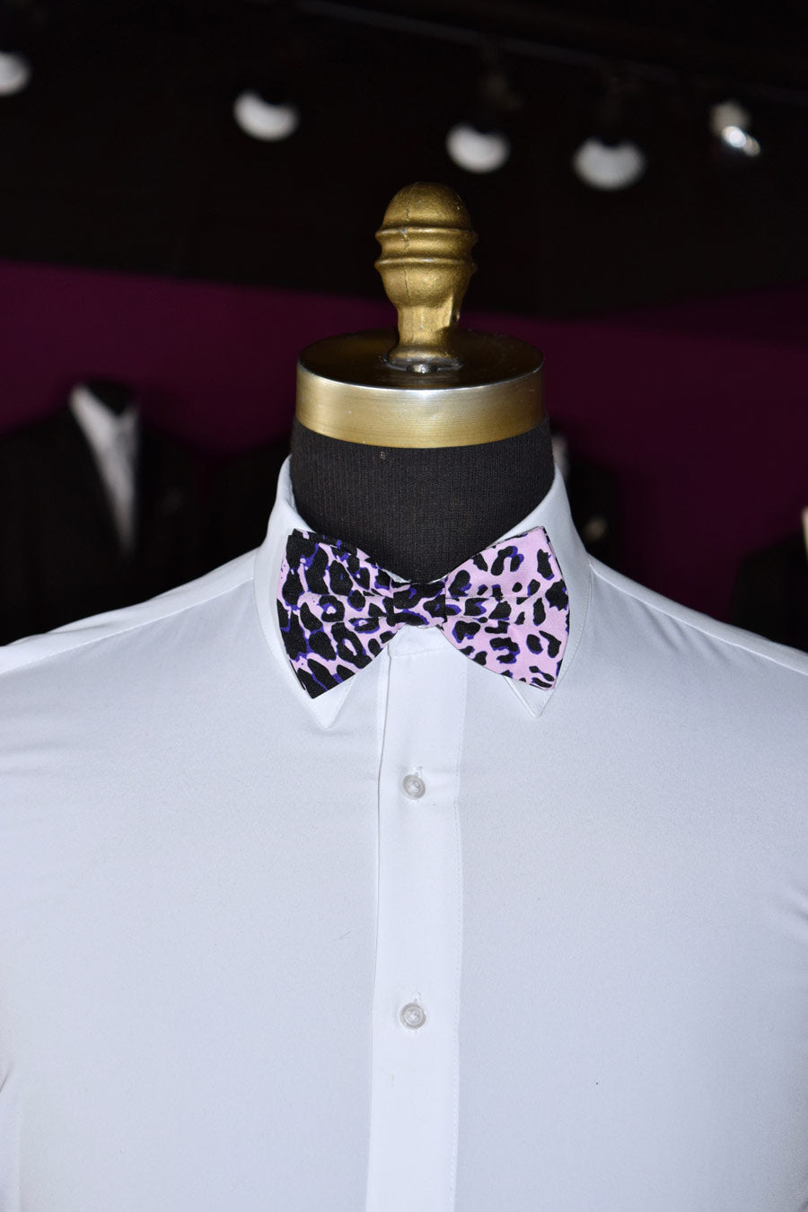 White shirt with a pink and purple leopard print bow tie on a mannequin against a dark background