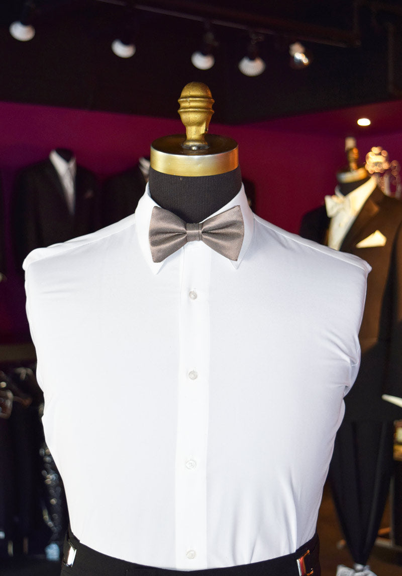 Mannequin wearing a white dress shirt with a stone colored bow tie inside a tuxedo shop with other mannequins in the background