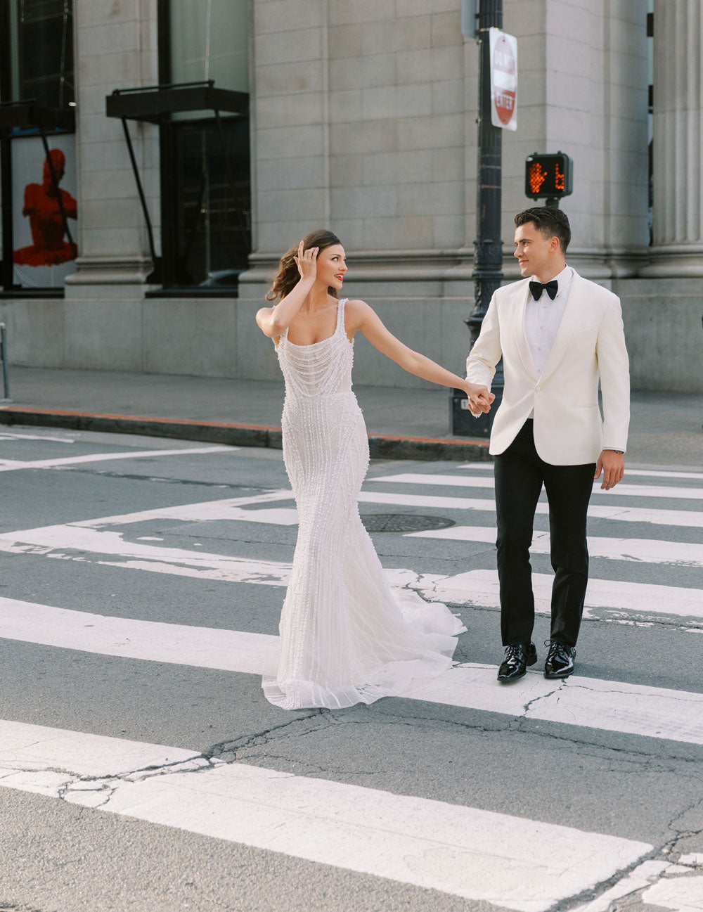 Groom wearing an ivory shawl collar tuxedo and a bride wearing an ivory wedding gown, crossing the street in downtown San Francisco. 