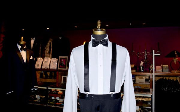 mannequin wearing a white tuxedo shirt with a black bowtie and black suspenders on display in a tuxedo shop