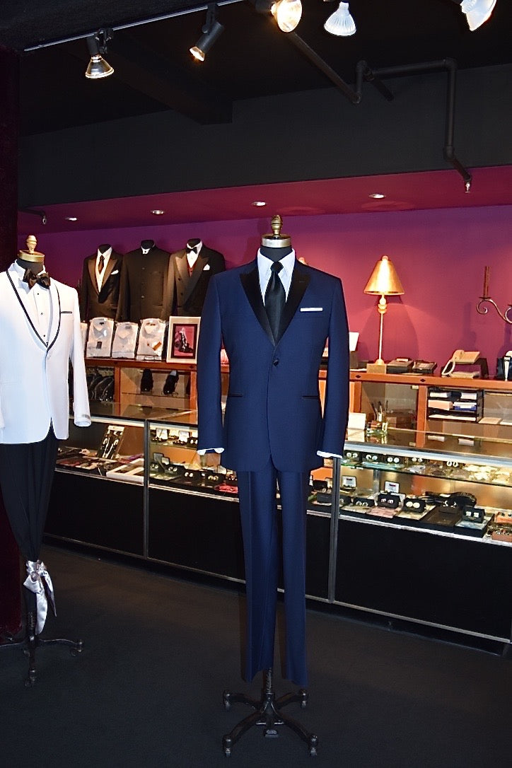 life size mannequin wearing a Blue peak-lapel tuxedo with a white dress shirt and black silk necktie in a store setting 