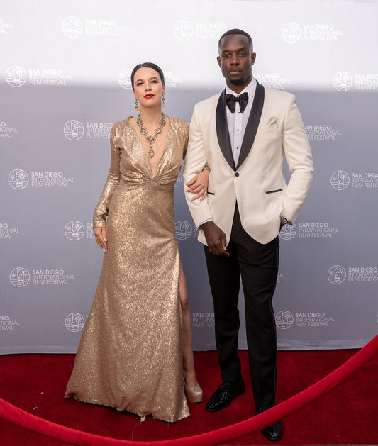 Man wearing a ivory tuxedo with a black butterfly and woman on a red carpet at the San Diego International Film