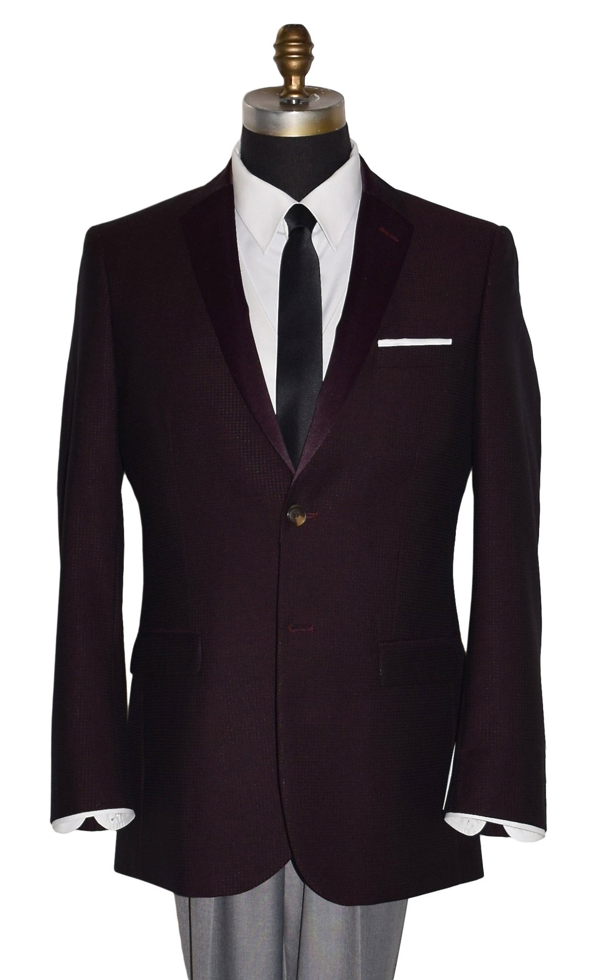 close-up  life size mannequin wearing a burgundy tuxedo jacket with a white tuxedo shirt and a long black skinny necktie against a white background