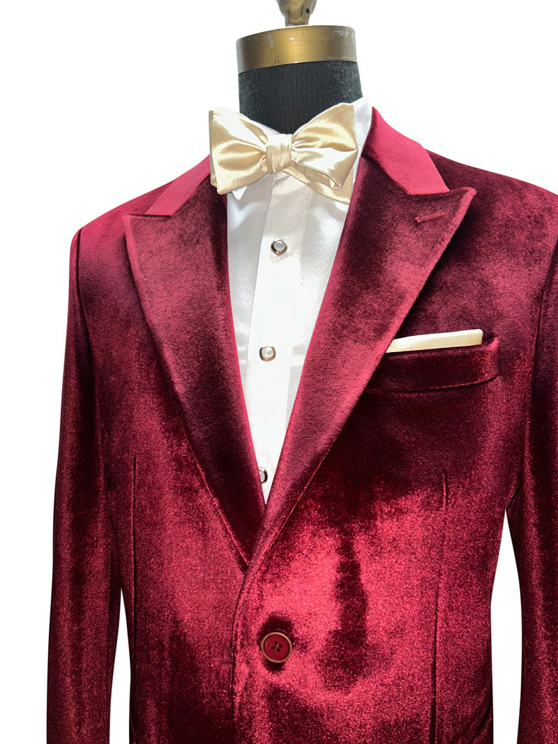 close up of a burgundy crimson red velvet dinner jacket with peak lapels with a champagne bowtie against a white background