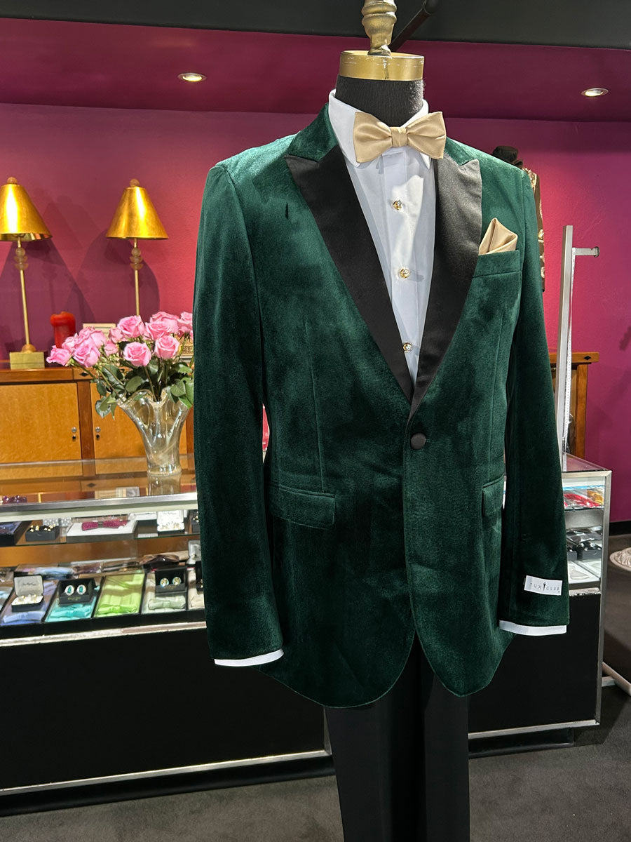 close up of a green velvet tuxedo on a mannequin with a white shirt and gold bowtie in store with suits on display