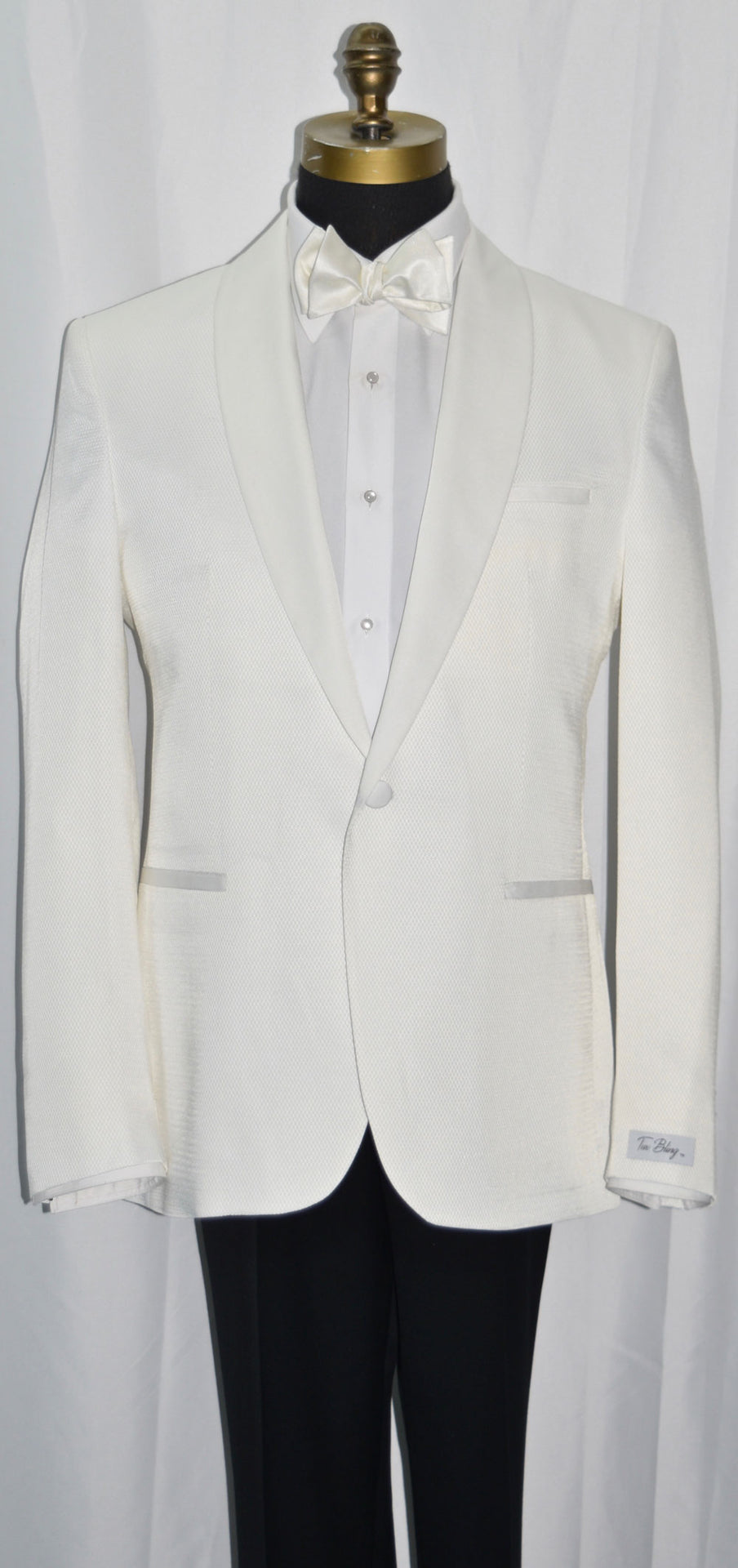 close-up life size mannequin mannequin wearing an ivory shawl collar tuxedo with a white tuxedo shirt and a ivory tie-yourself bowtie against a white background