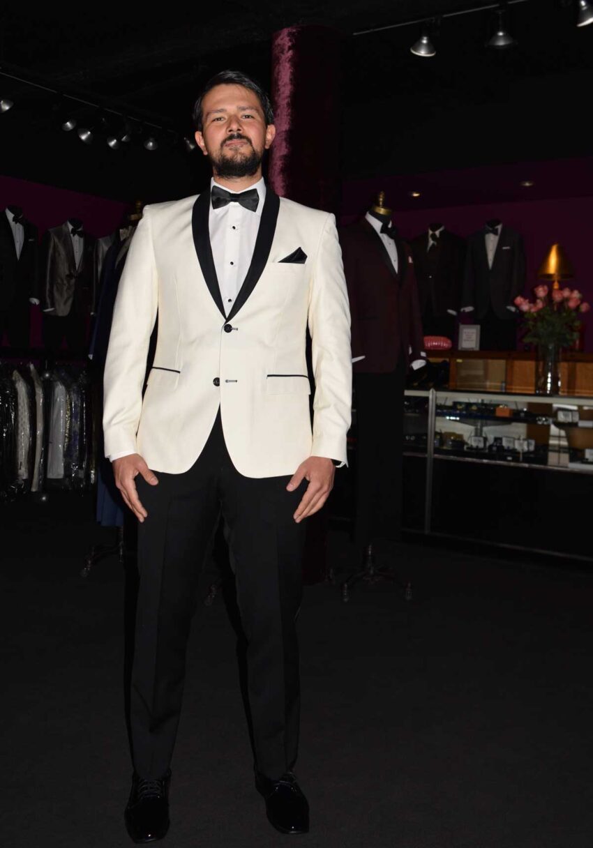 Man wearing an ivory tuxedo with a black shawl collar in a tuxedo shop.