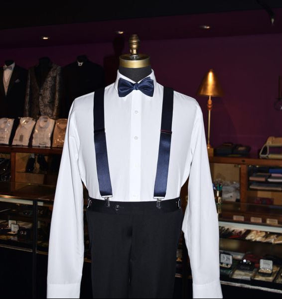 mannequin wearing a white dress shirt with marine blue bowtie and suspenders in a tuxedo shop