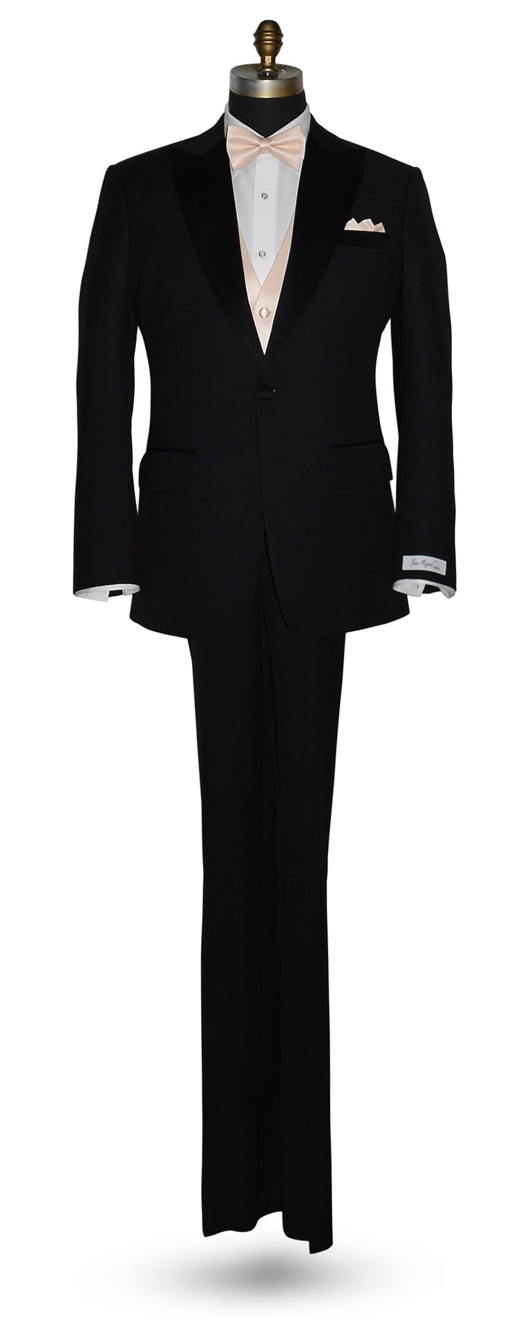 life-size mannequin wearing a black peak-lapel tuxedo with a "San Miguel Especial" branded label wearing a white shirt with a nude tuxedo vest and a nude bow tie against a white background