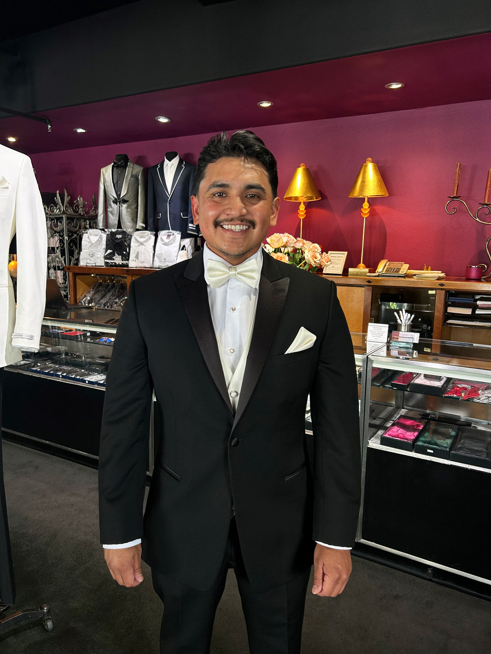 groom wearing a black tuxedo with an off-white bowtie and vest inside a tuxedo shop