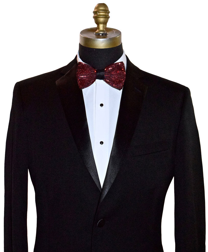 Black tuxedo with a white shirt and red sequin bow tie on a mannequin against a white background.