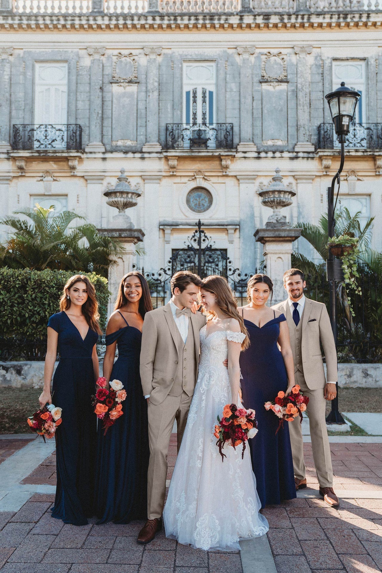 group photo of a wedding party where the men are wearing the sand suit, with  bridesmaids wearing long navy blue gowns.