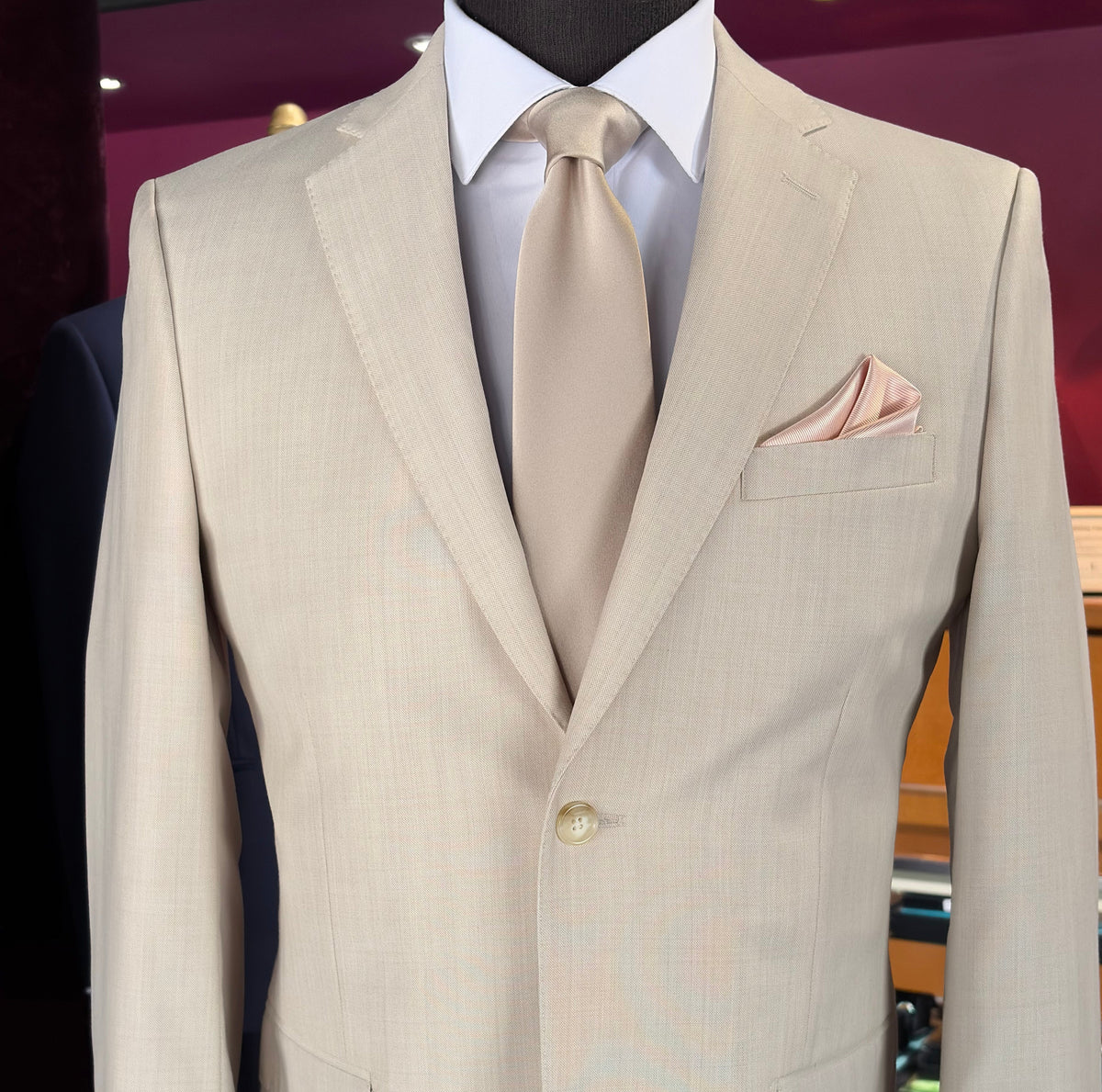 close-up mannequin wearing a tan fitted suit with a champagne necktie and a blush pocket handkerchief. 