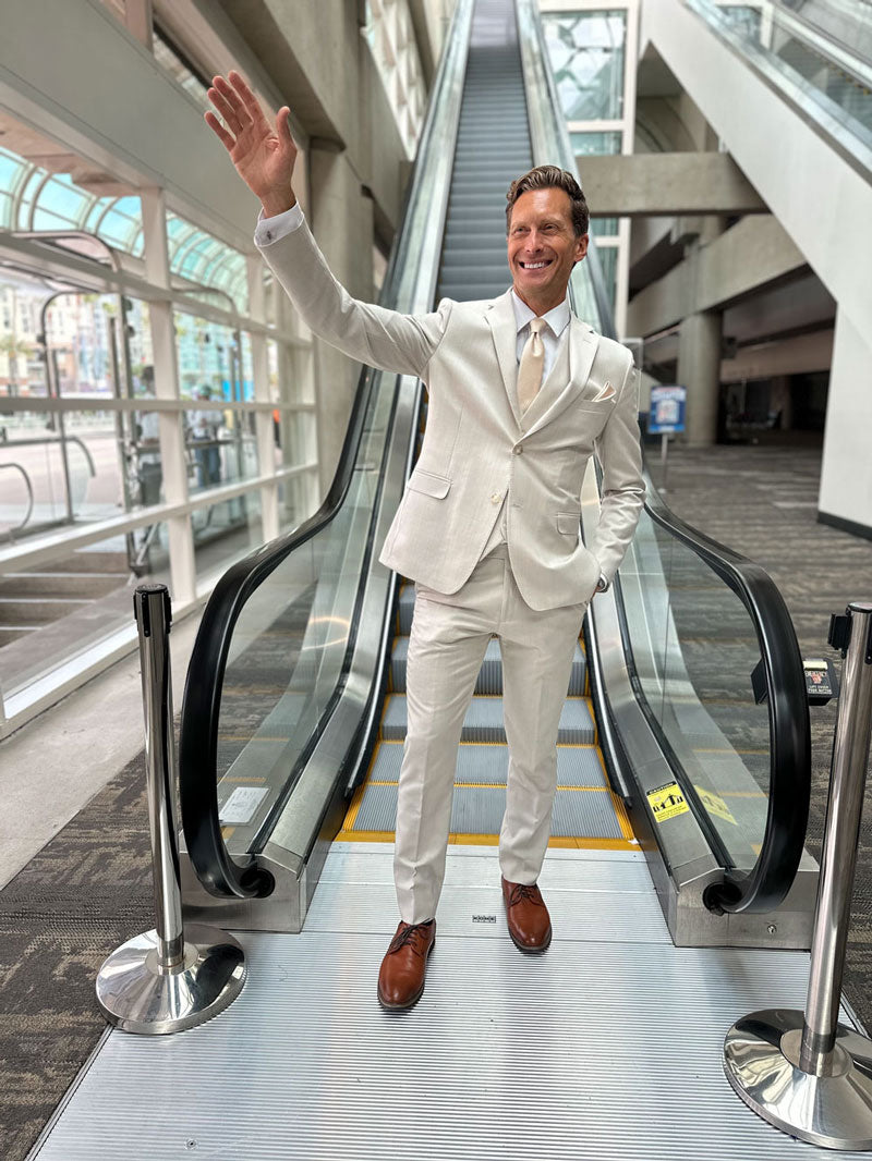 Model wearing a Tan slim fit 3 piece suit from TUXCLUB with brown shoes and champagne tie coming down an escalator. 