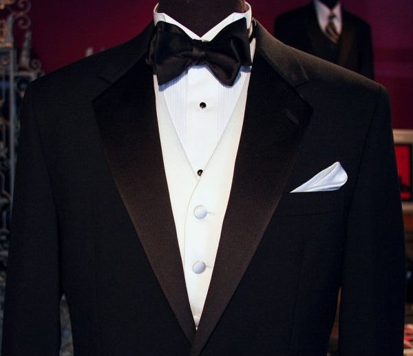close-up Black tuxedo with white shirt and white satin tuxedo vest with a black bow tie on a mannequin against a red background